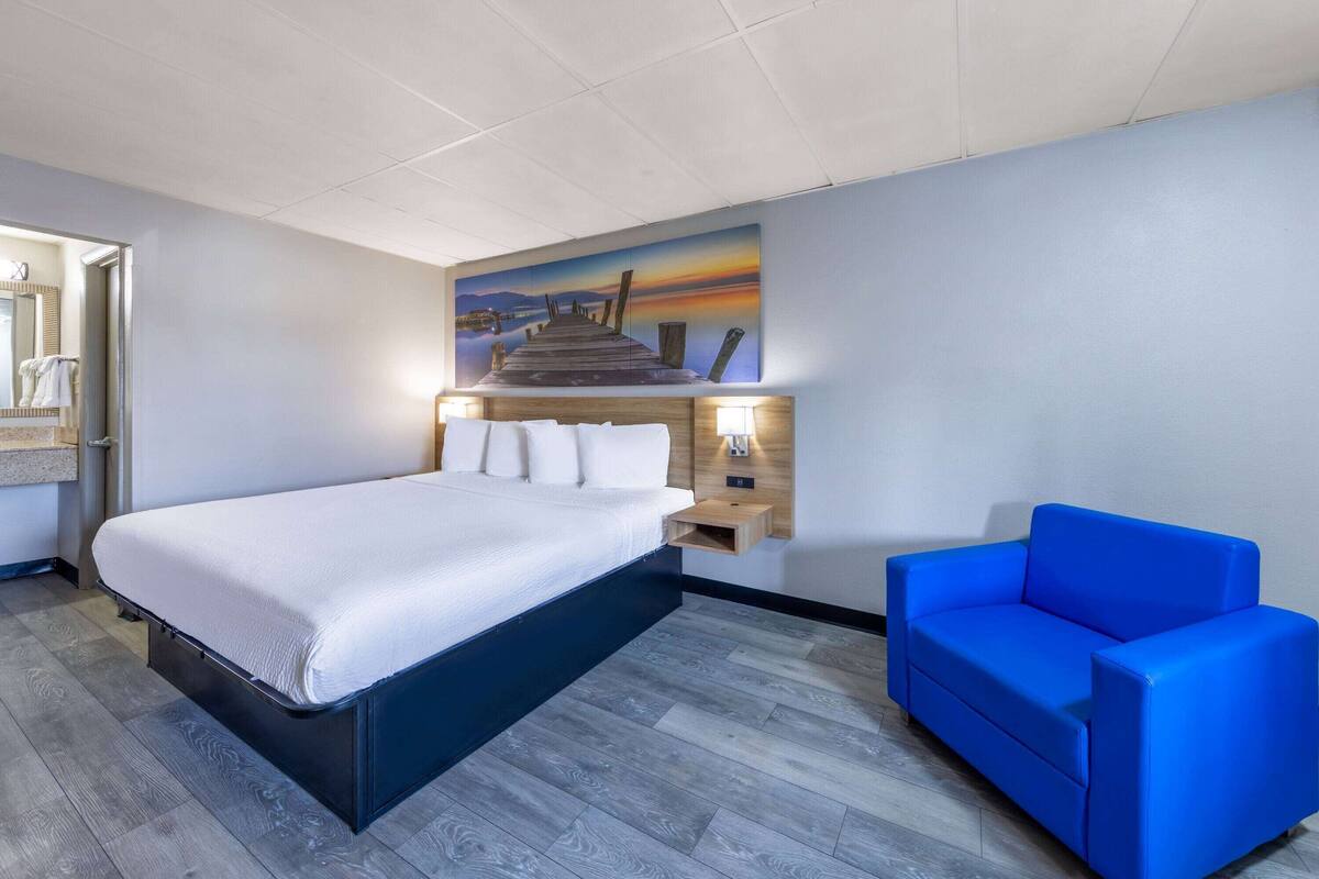 Ein Hotelzimmer mit einem Bett, einem blauen Sofa, einem Gemälde eines Piers und einem Nachttisch mit einer Lampe.