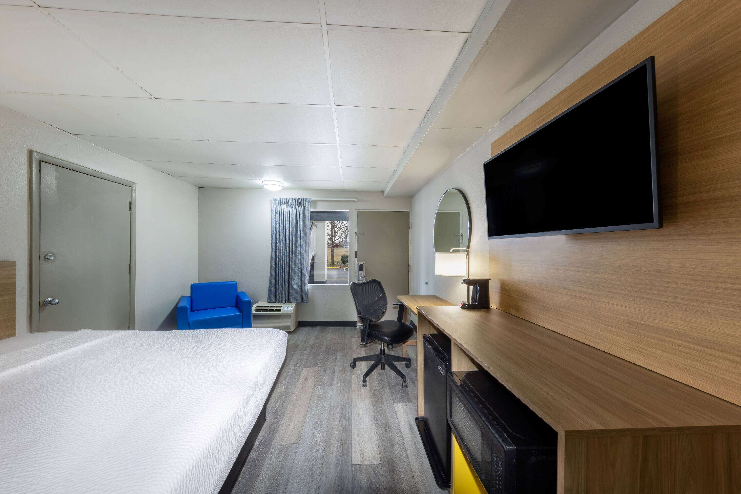 A hotel room with a bed, desk, chair, TV, and a mirror.