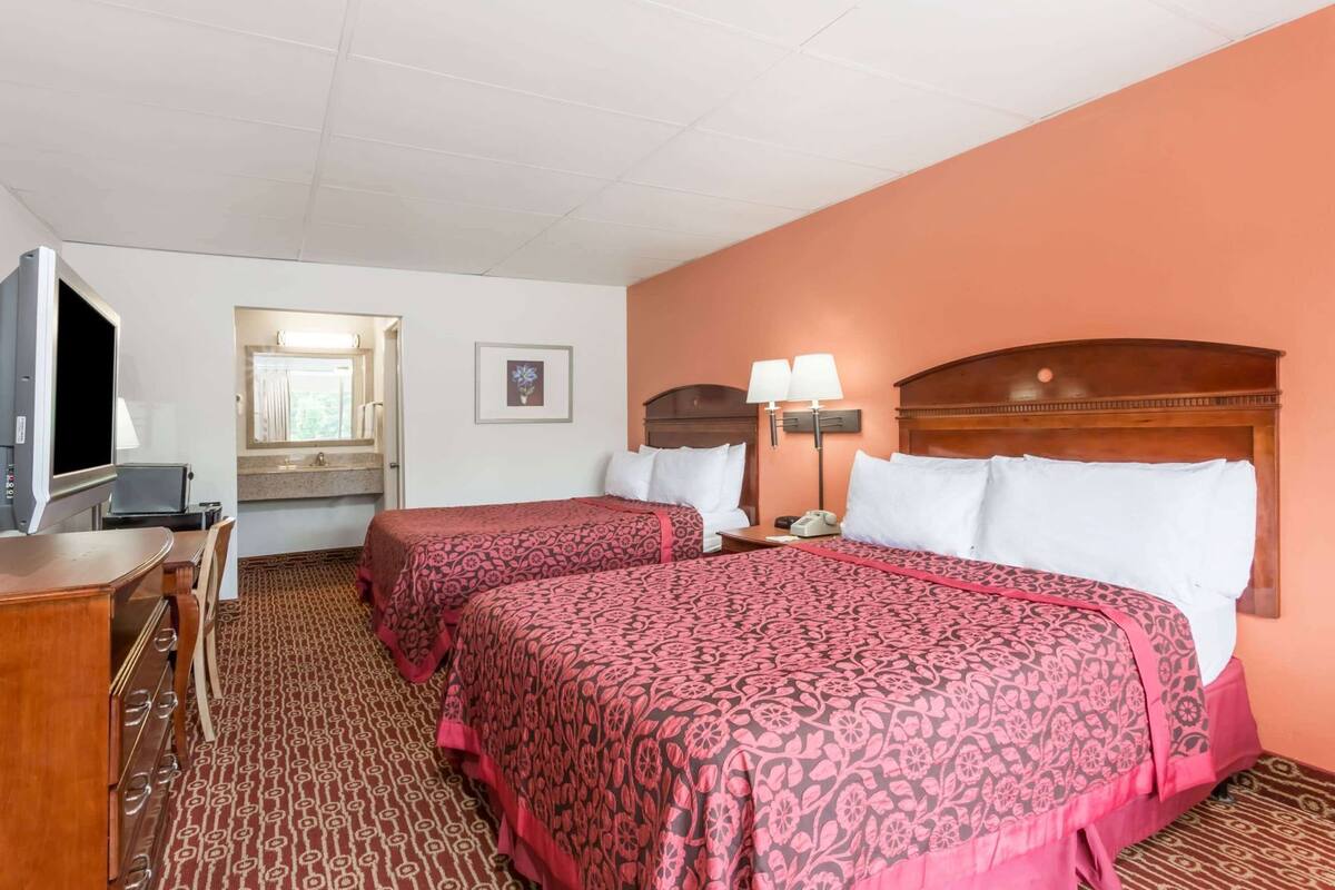 Ein Hotelzimmer mit zwei Betten, einem Schreibtisch, einem Fernseher und einem durchgegangenen Badezimmer.