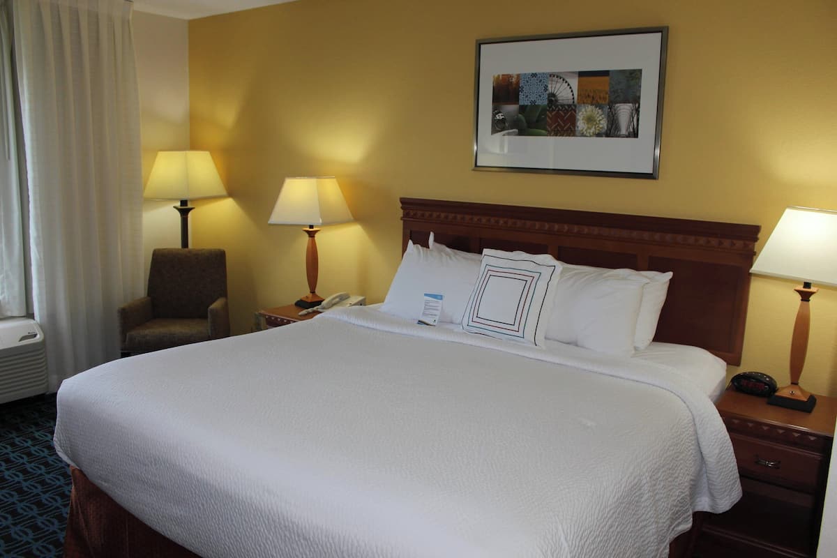 Habitaci ón de hotel con una cama grande, dos lámparas de noche, una silla, mesita de noche con teléfono y un cuadro en la pared.