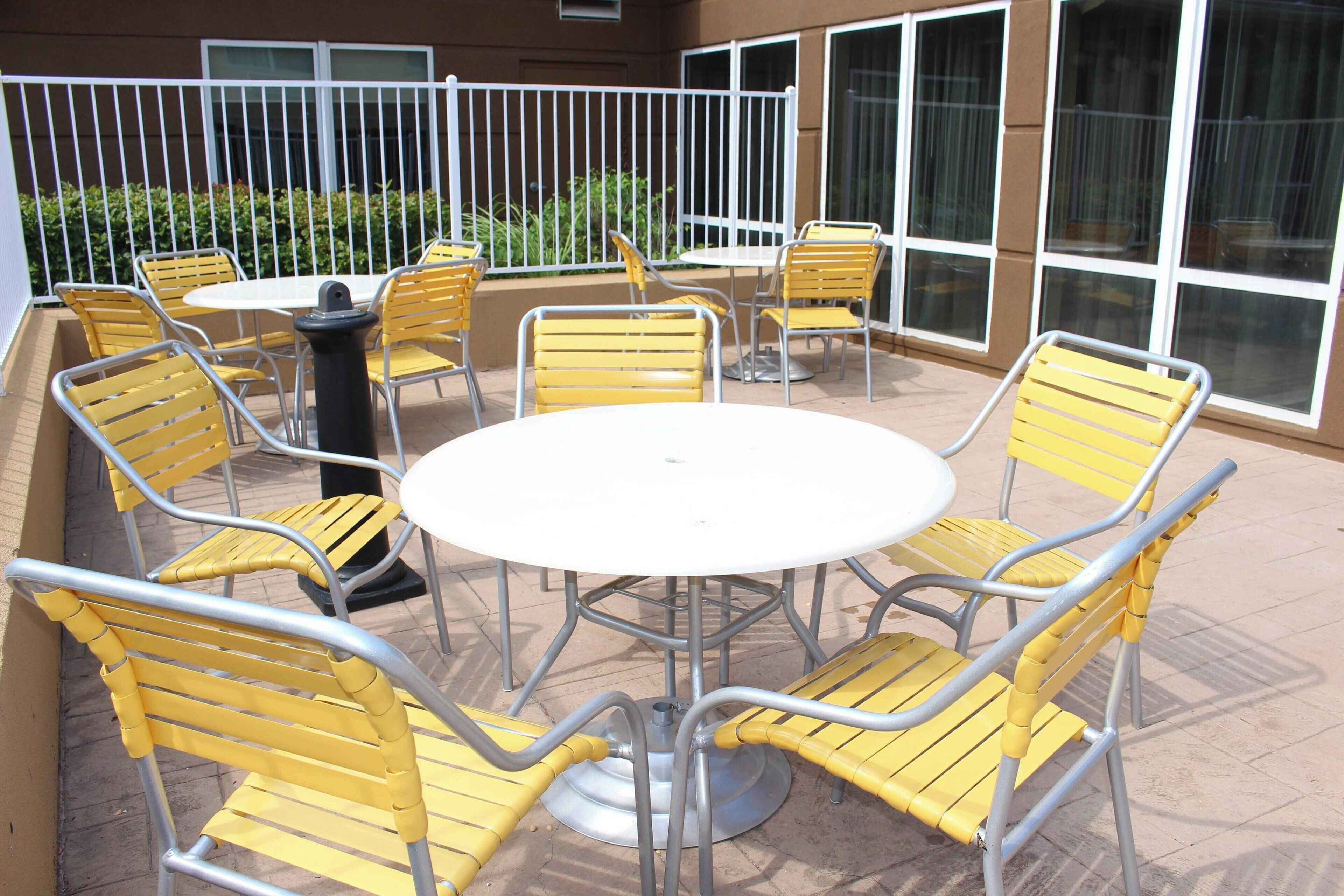 Une terrasse extérieure avec des chaises en métal jaune et une table blanche, le tout entouré d’une clôture en métal blanc.