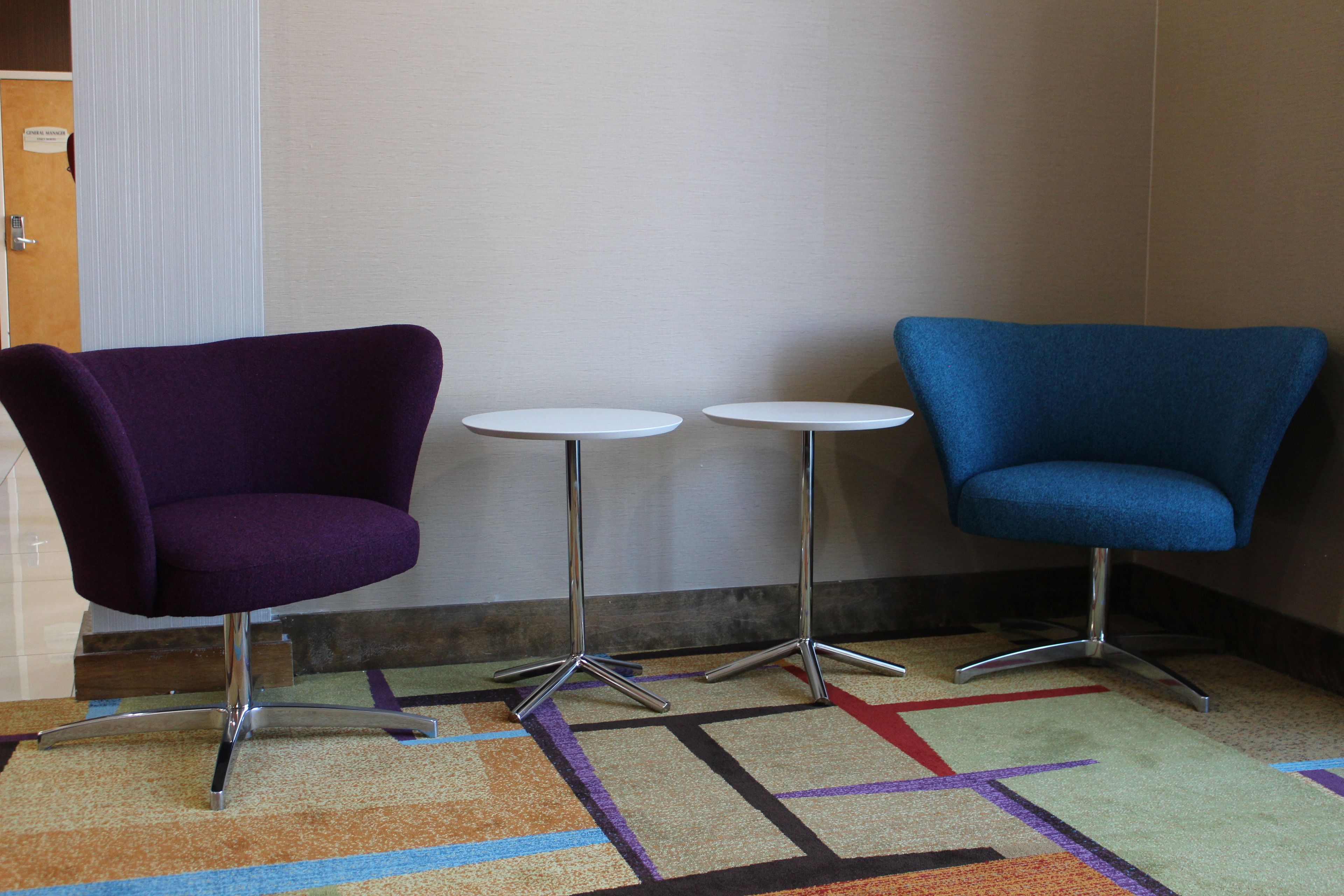 A room with two small round tables and two chairs, one purple and one blue, with a patterned carpet.
