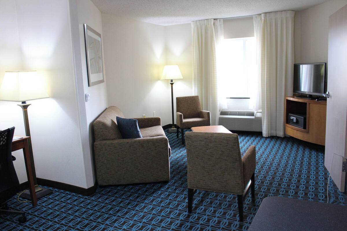 Habitación de hotel con sofá, sillón y televisor sobre un mueble de madera.