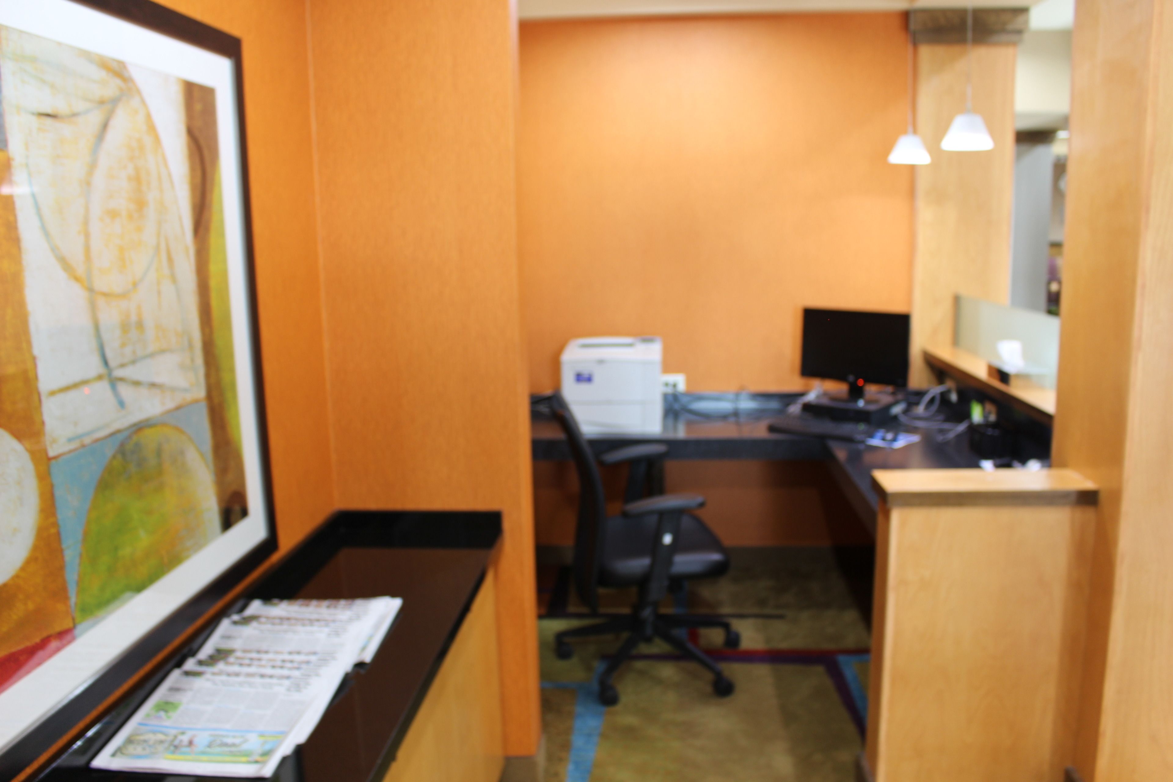 Une pièce comprenant un bureau, un fauteuil de bureau, un ordinateur et un tableau abstrait encadré accroché au mur.
