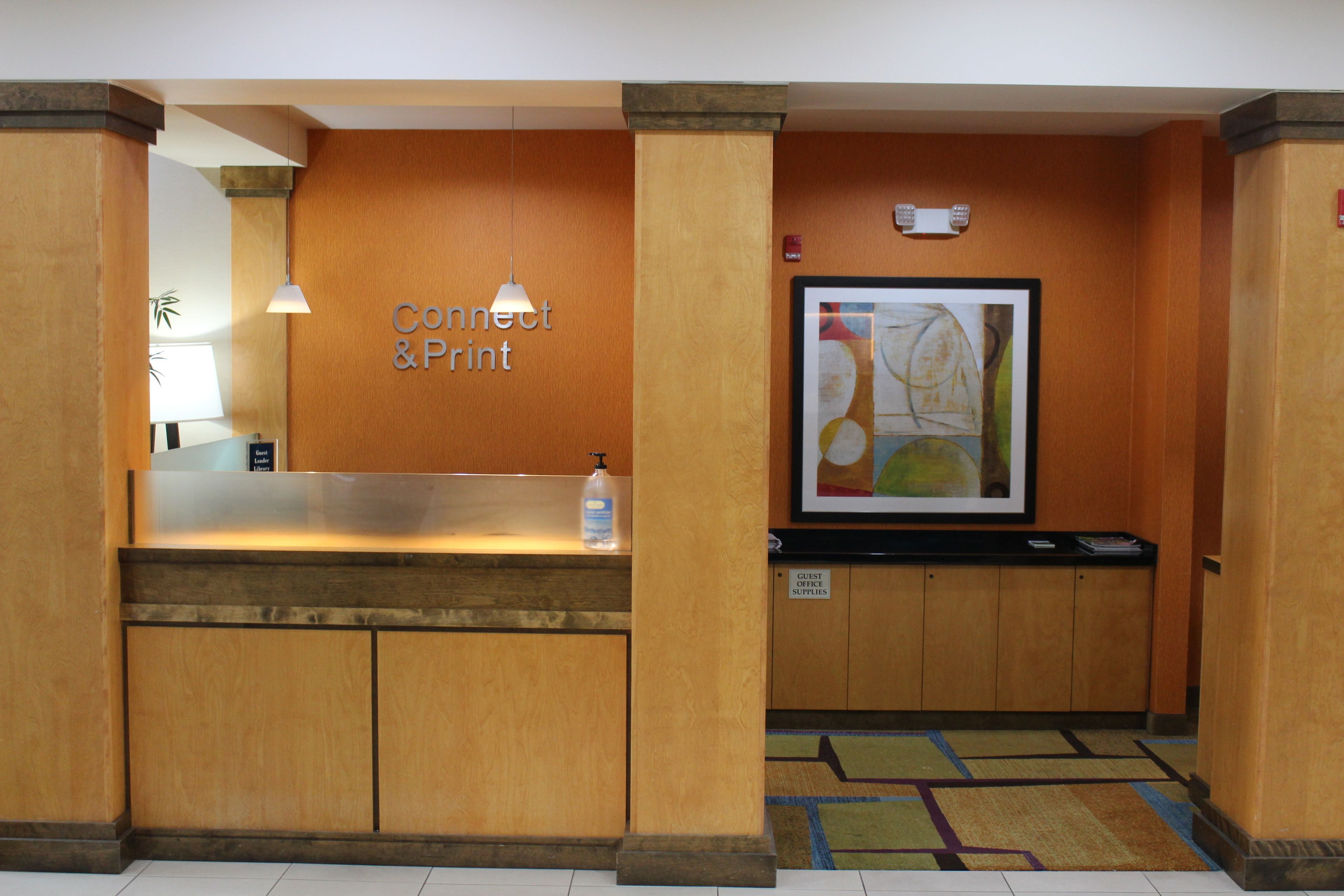 A reception area with a wooden reception desk, a sign reading "Connect & Print", and a framed abstract painting on the wall.