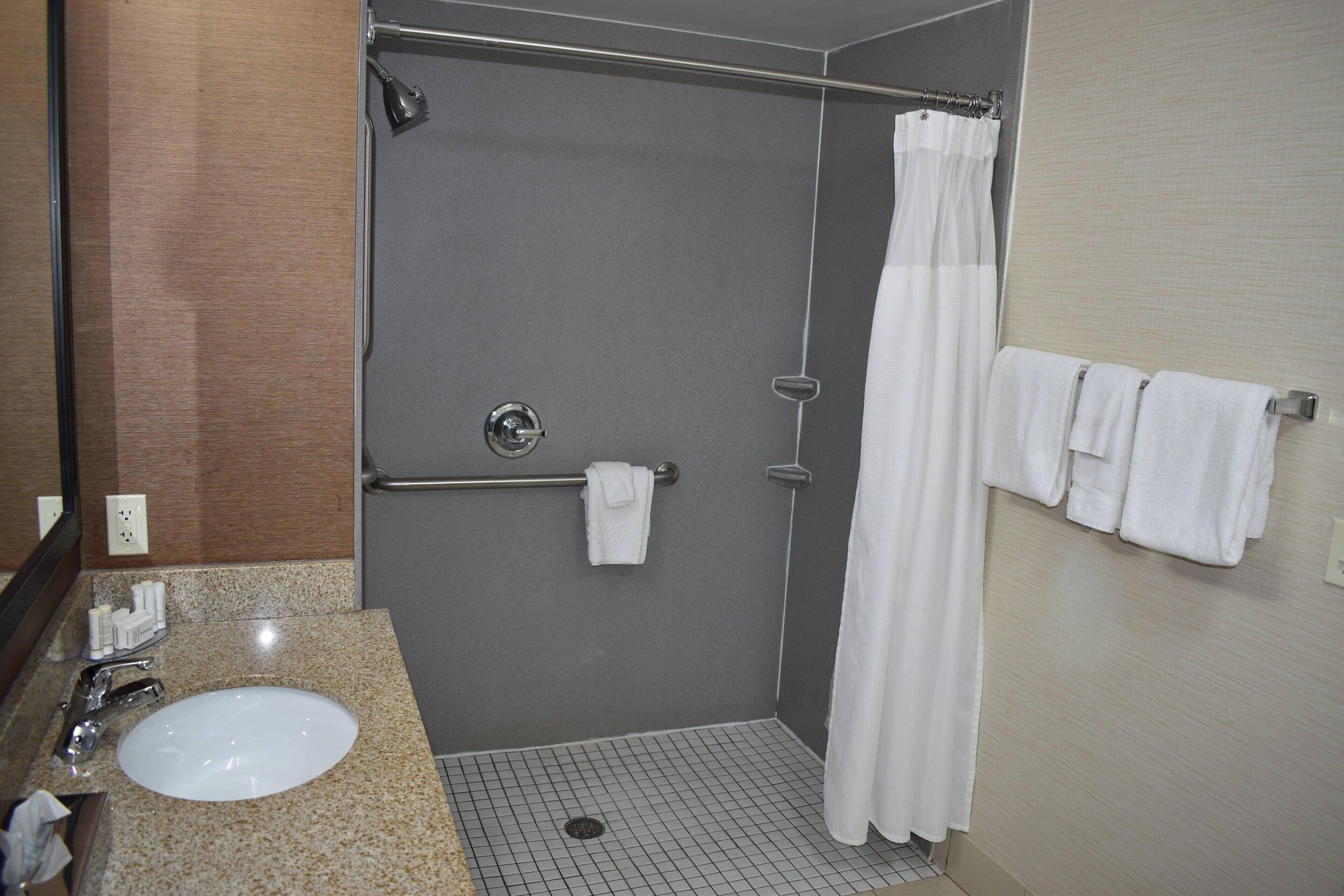 A bathroom with a sink, mirror, shower, and towel rack.