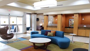 Un hall d’hôtel moderne avec un canapé bleu, une table basse ronde et un fauteuil en cuir marron.