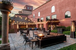 Un espacio al aire libre con zona de estar, luces colgantes y una chimenea.