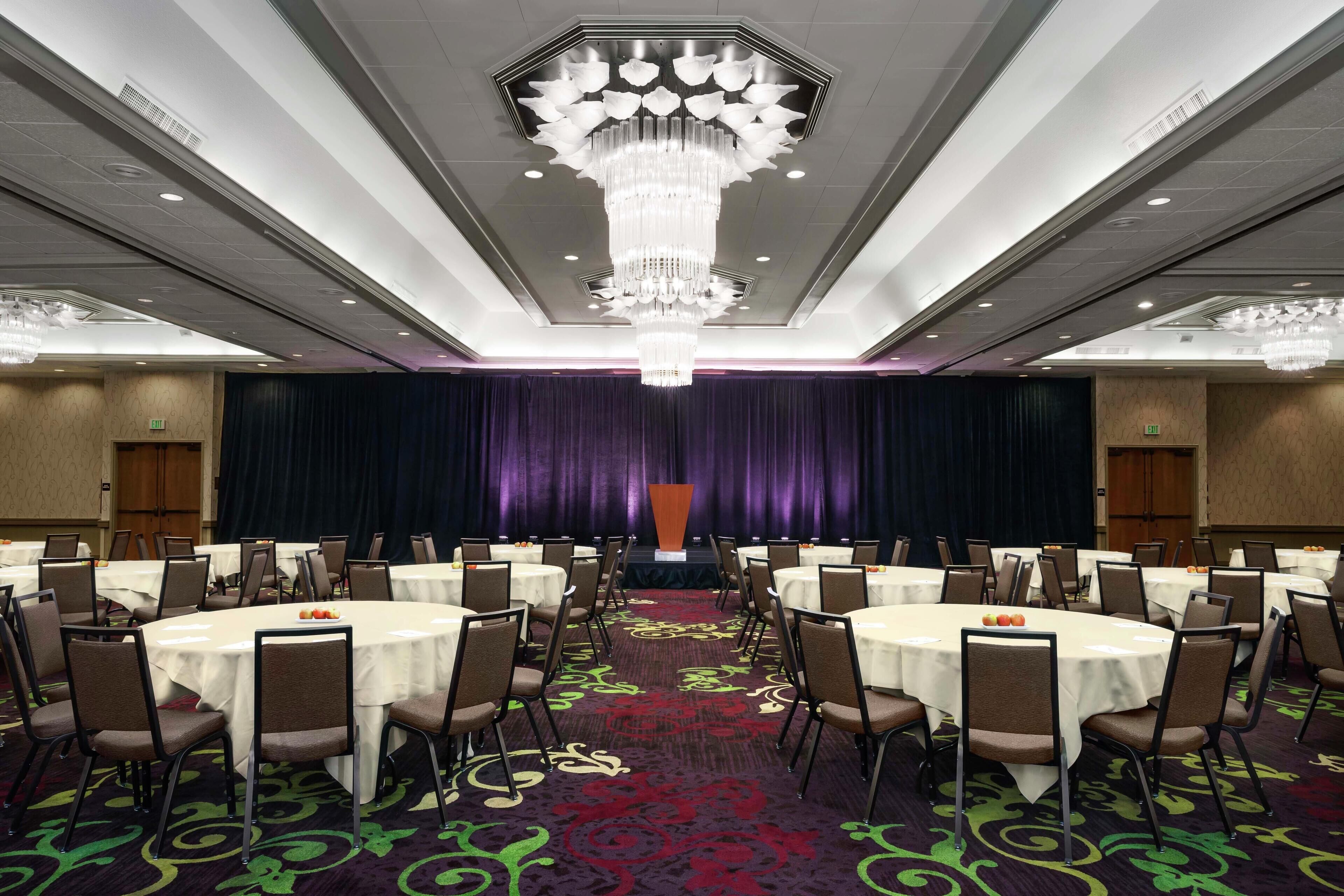 A conference room with round tables, chairs, and a large chandelier.