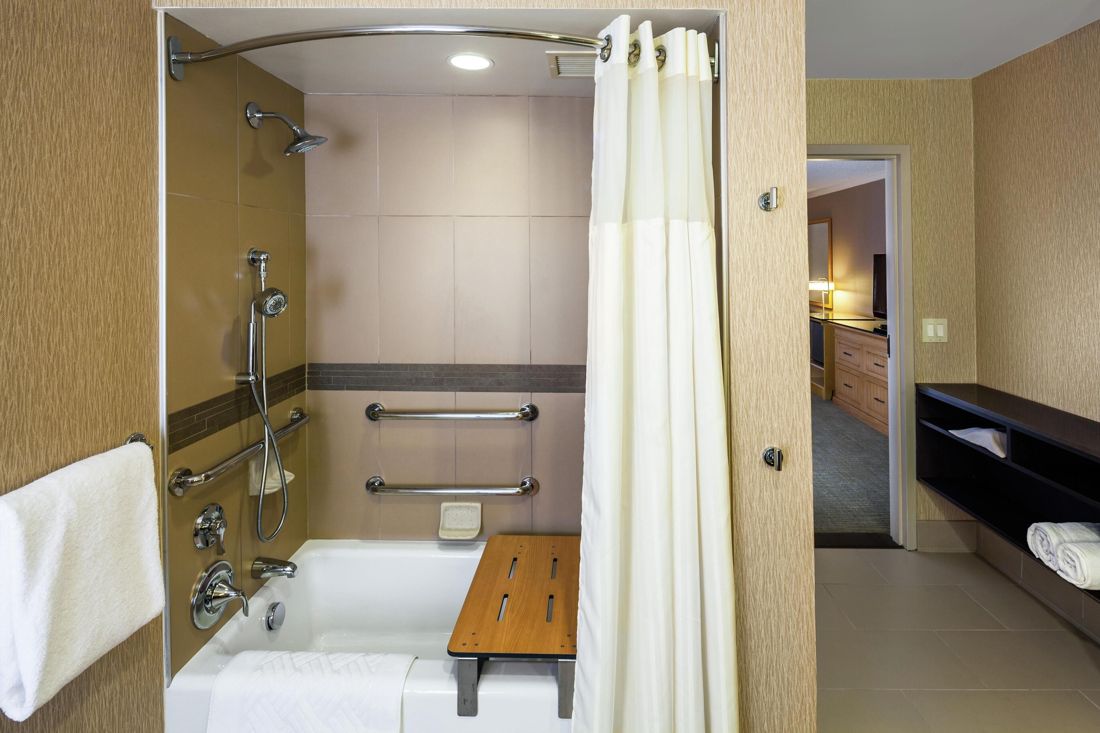Un baño moderno con ducha, bañera, un taburete de madera y un perchero para toallas.