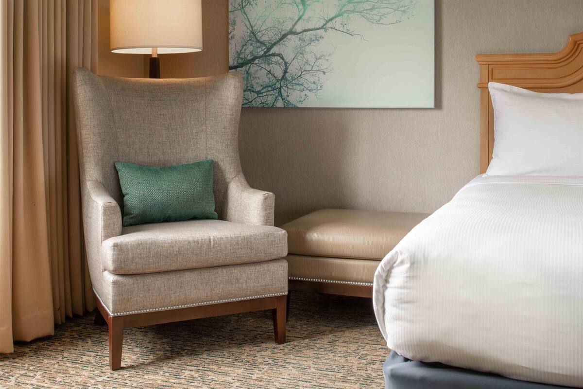 Une chambre d’hôtel avec un grand lit, une chaise avec un coussin vert, une lampe et une œuvre d’art murale.