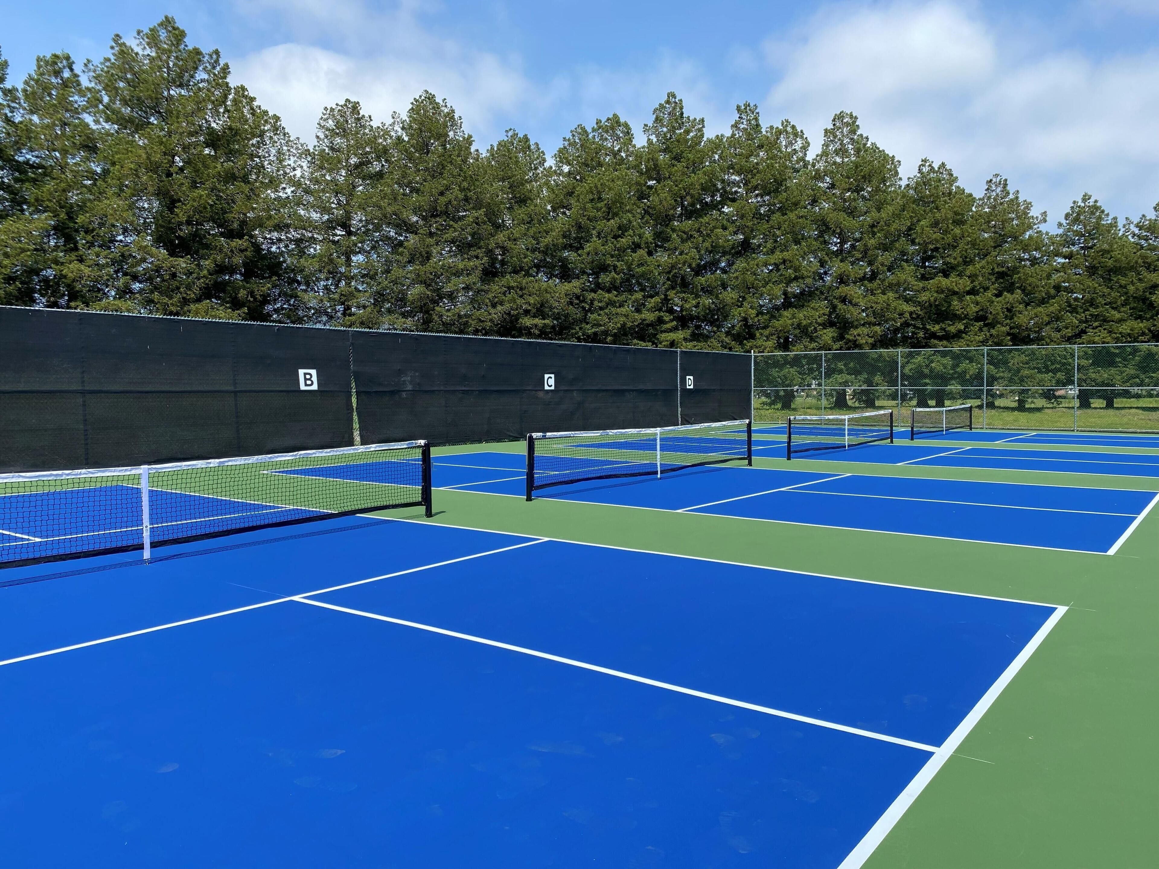 A tennis court with multiple courts, a net, and a fence.