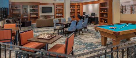 A hotel lobby with a pool table, seating area, and a television.