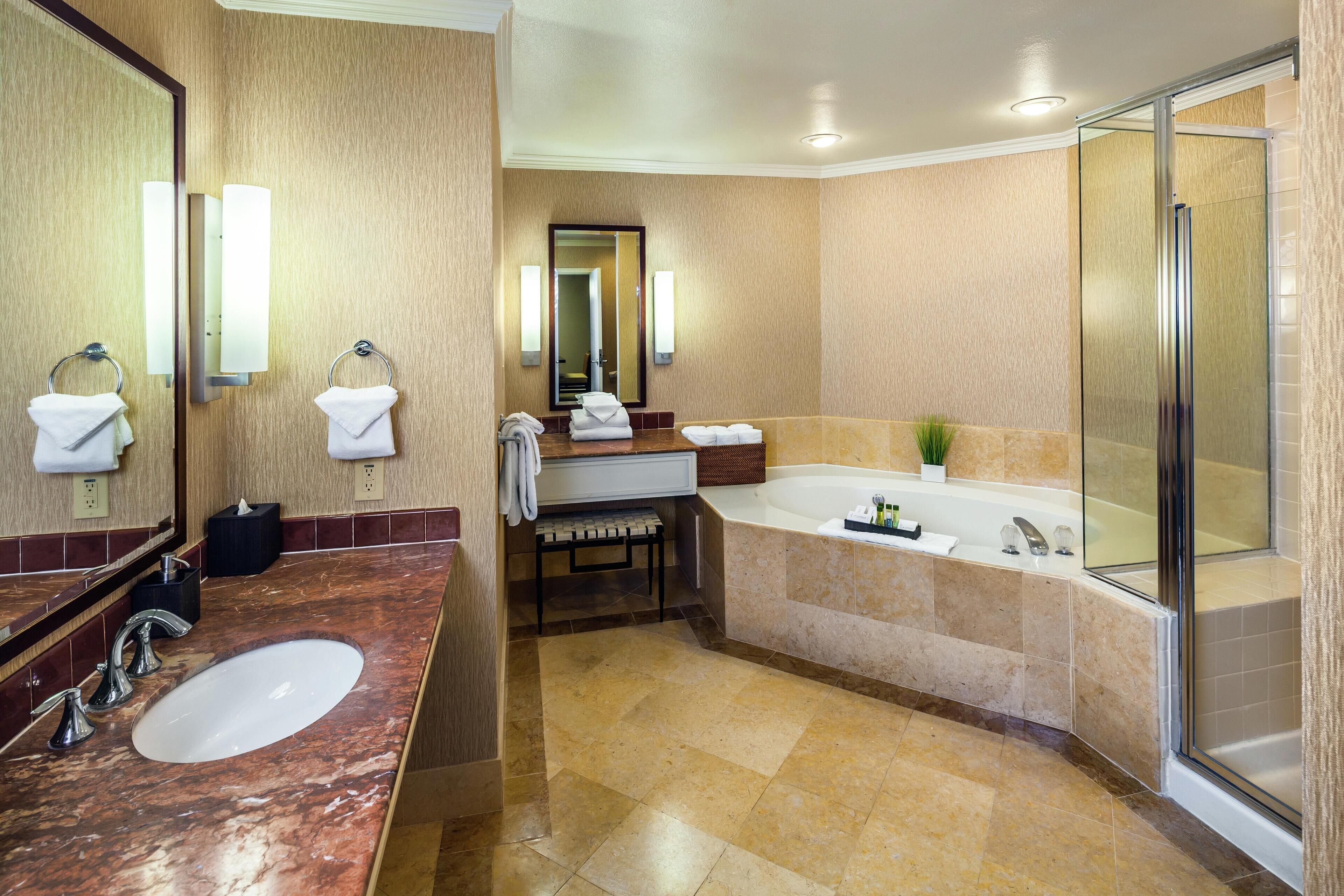 A modern bathroom with a marble vanity, a large mirror, a bathtub, and a glass-enclosed shower.