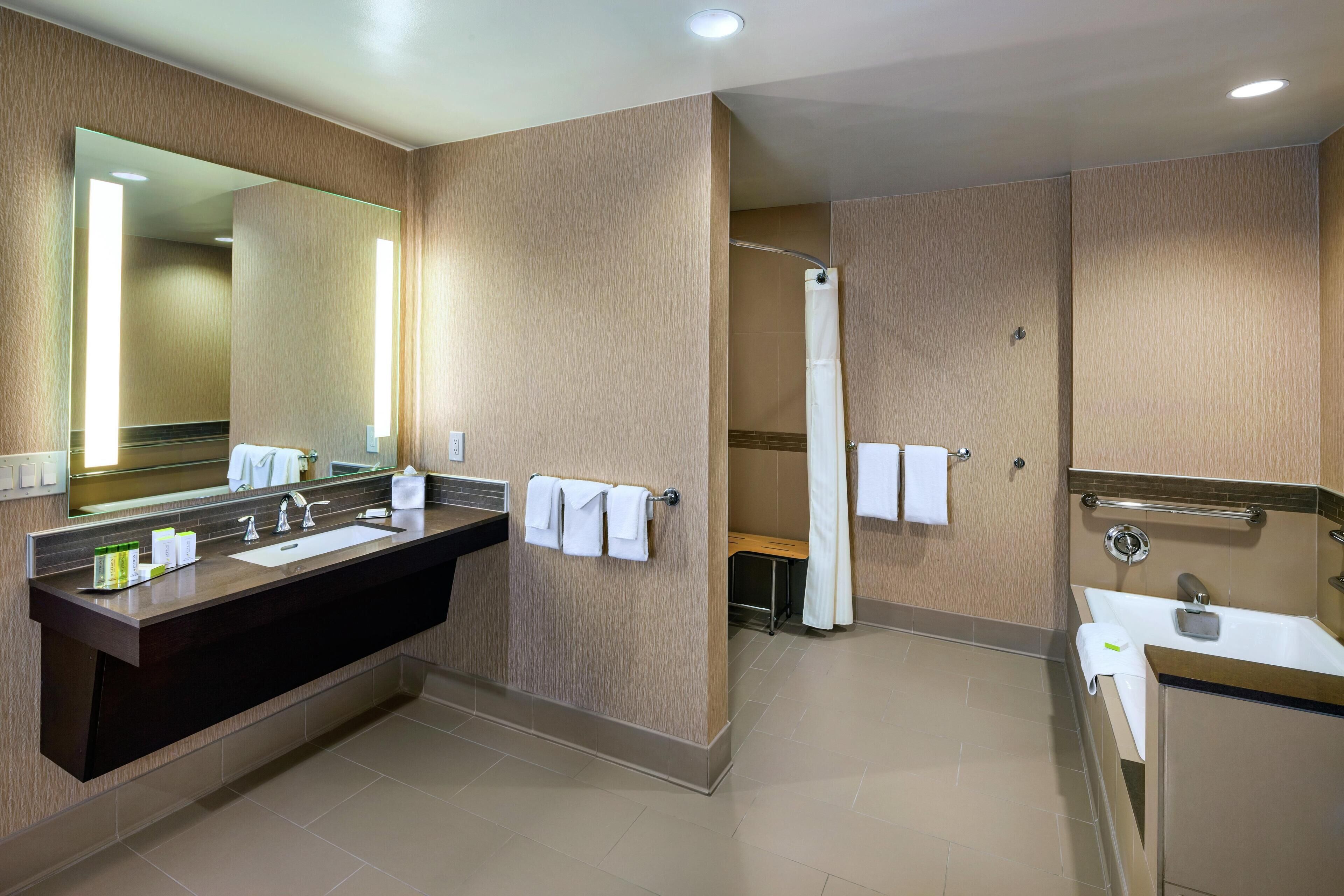 A modern bathroom with a large mirror, a dark vanity, a shower area, and a separate sink.
