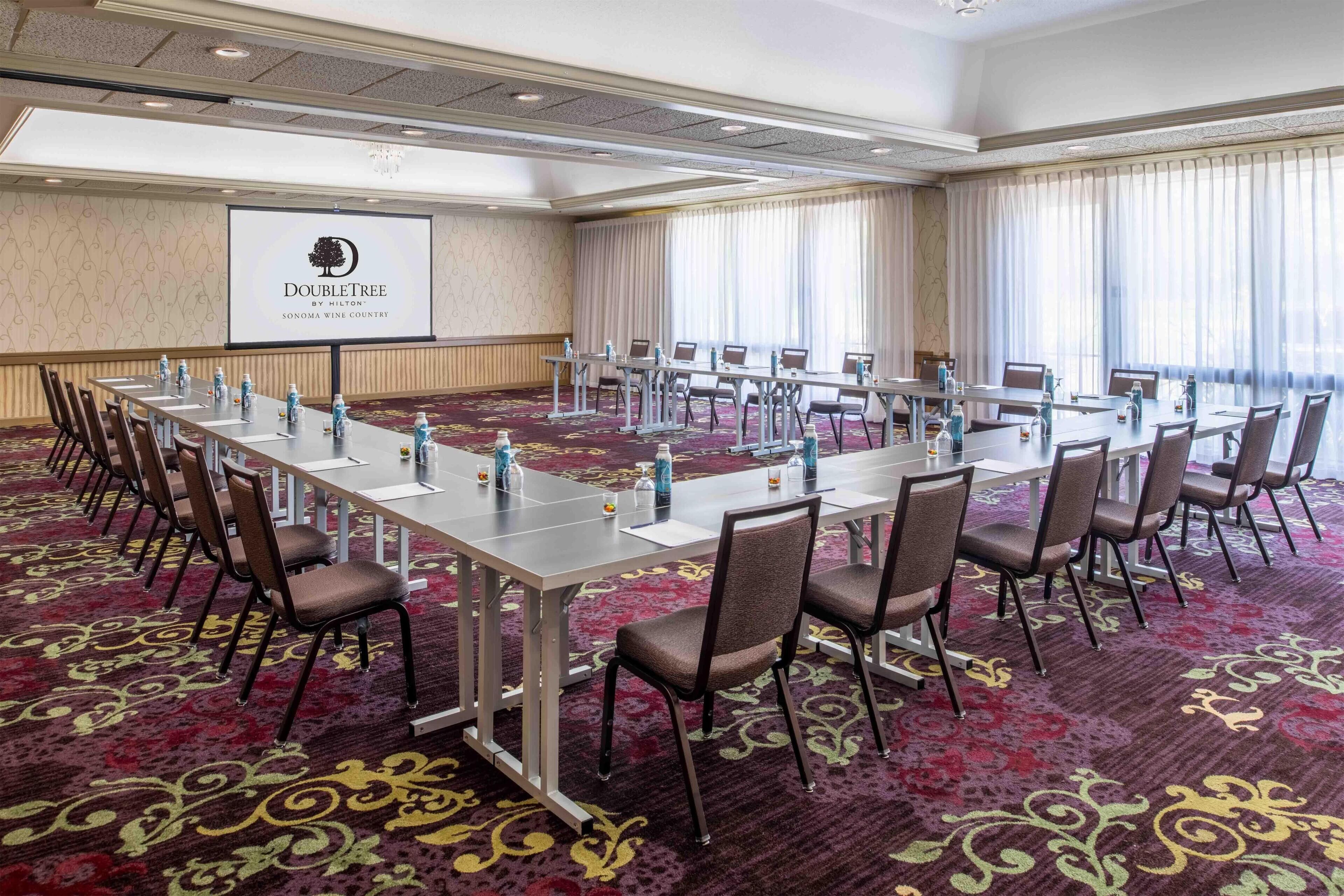 Un salón de conferencias con una larga mesa, sillas y una pantalla de proyector que muestra el logo de DoubleTree.