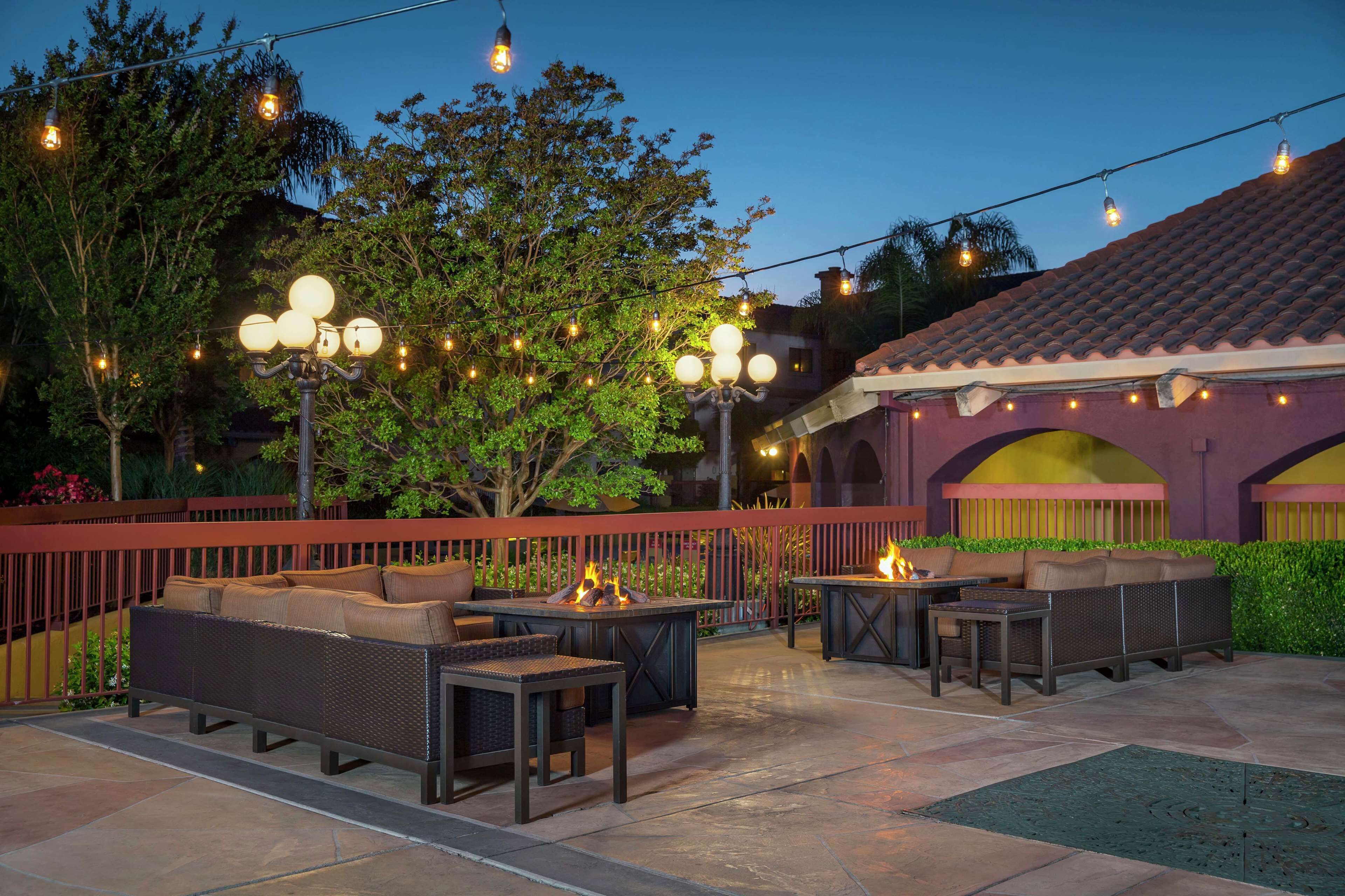 Un patio al aire libre con asientos, luces colgantes y una chimenea.