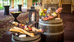 A buffet setup with various cheeses, fruits, and meats on wooden barrels and tables in a spacious room with a carpeted floor and large windows. - DoubleTree by Hilton Sonoma - Wine Country (Rohnert Park)