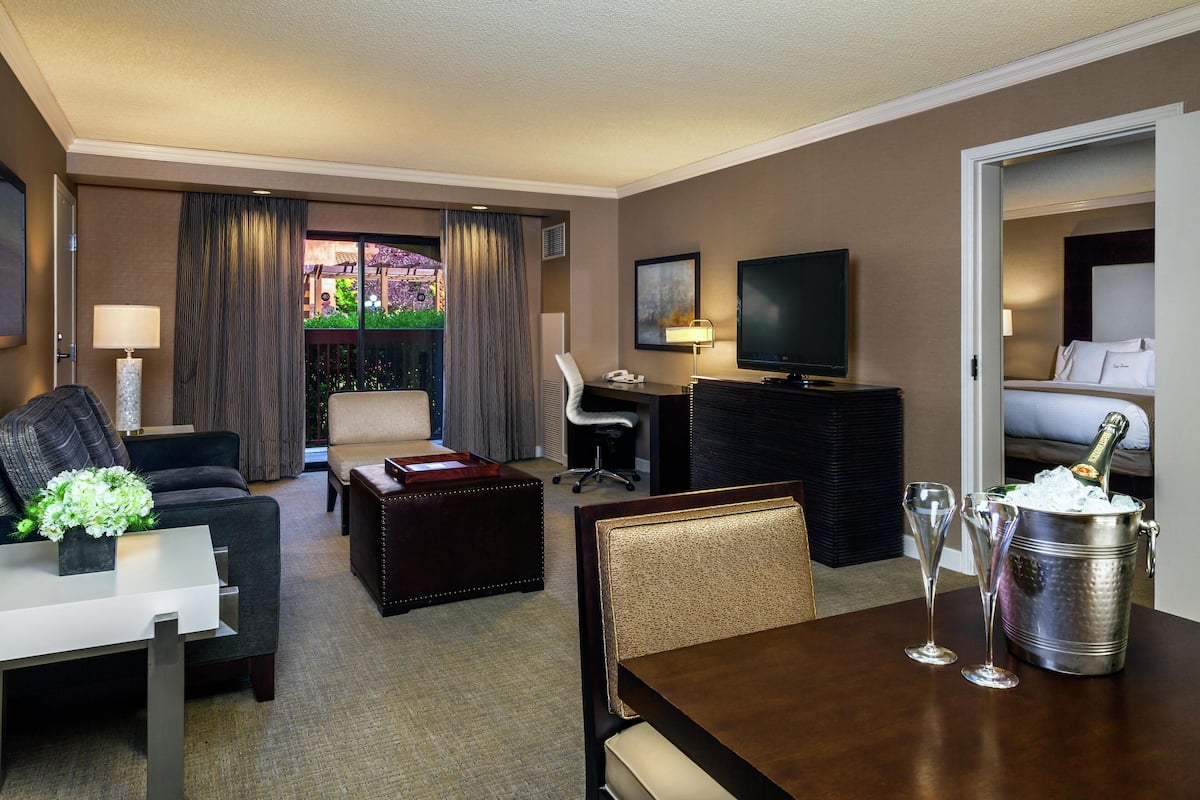 Une chambre d’hôtel équipée d’une table à manger, de deux chaises, d’un canapé, d’une télévision, d’un minibar et d’un balcon avec des rideaux.