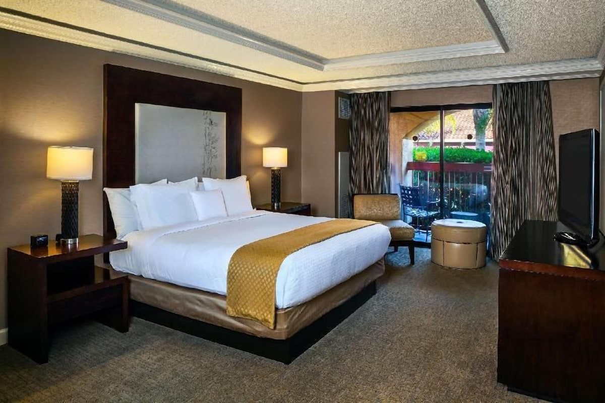 Une chambre d’hôtel avec un grand lit, deux tables de chevet, une chaise, un bureau et un téléviseur.