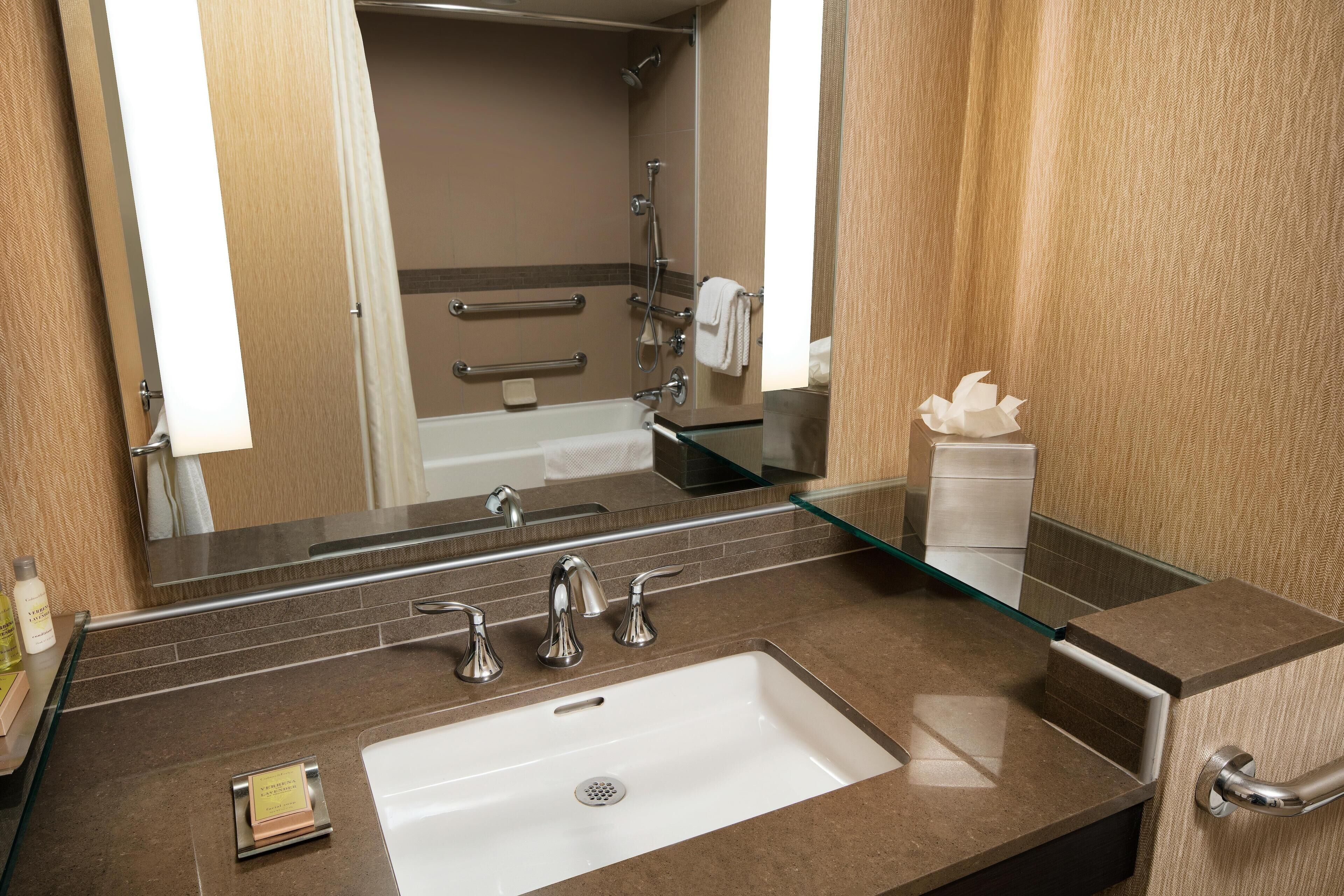 Une salle de bain avec un grand miroir, un lavabo blanc et une cabine de douche en verre.