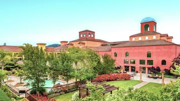 Stunning hotel with arched windows, a bell tower, and a blue dome atop a red building, set amidst beautifully maintained gardens and a swimming pool.
