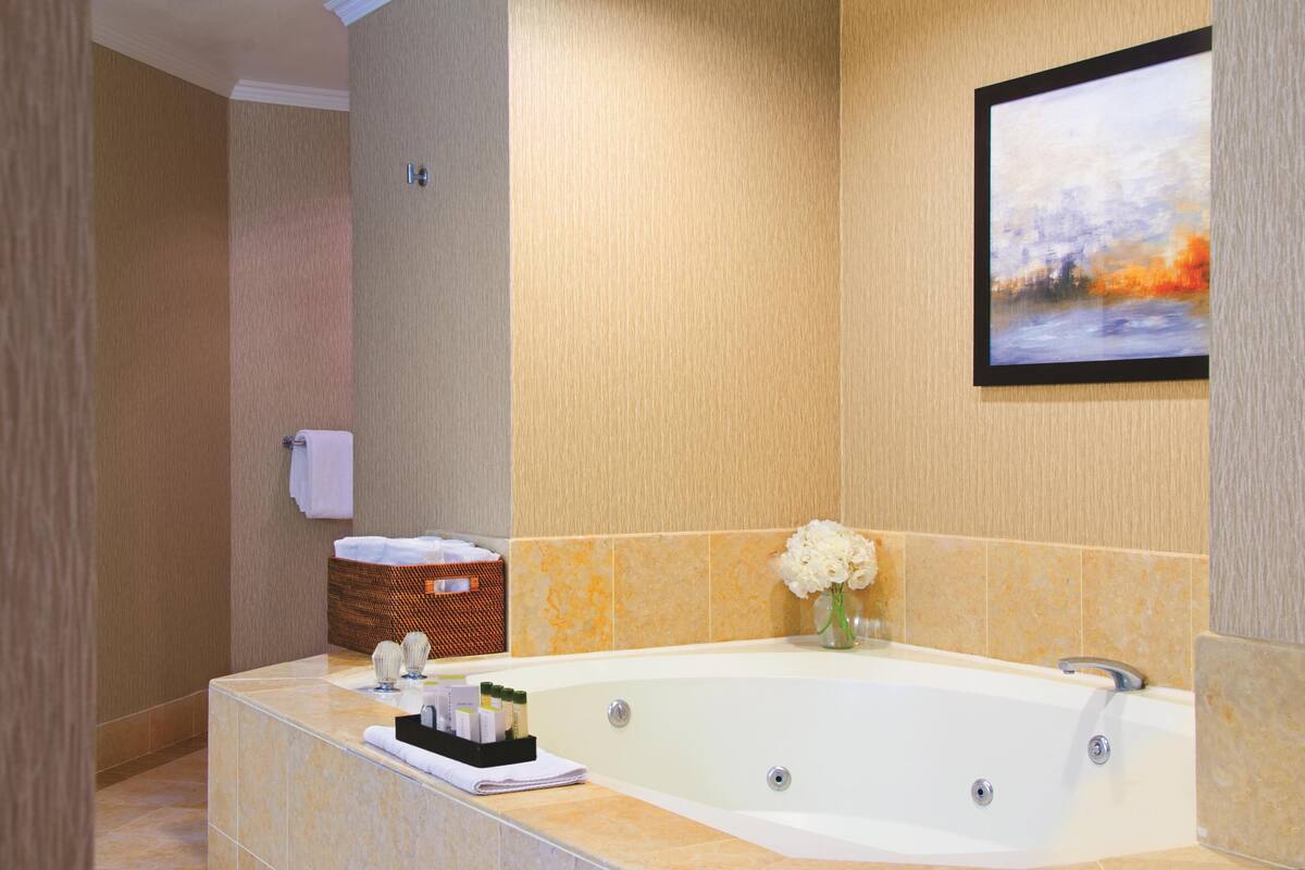Une salle de bain avec une grande baignoire, un tableau encadré au mur et un panier contenant des articles de toilette.