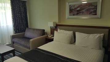 A hotel room with a bed, a chair, a nightstand, and a painting on the wall.