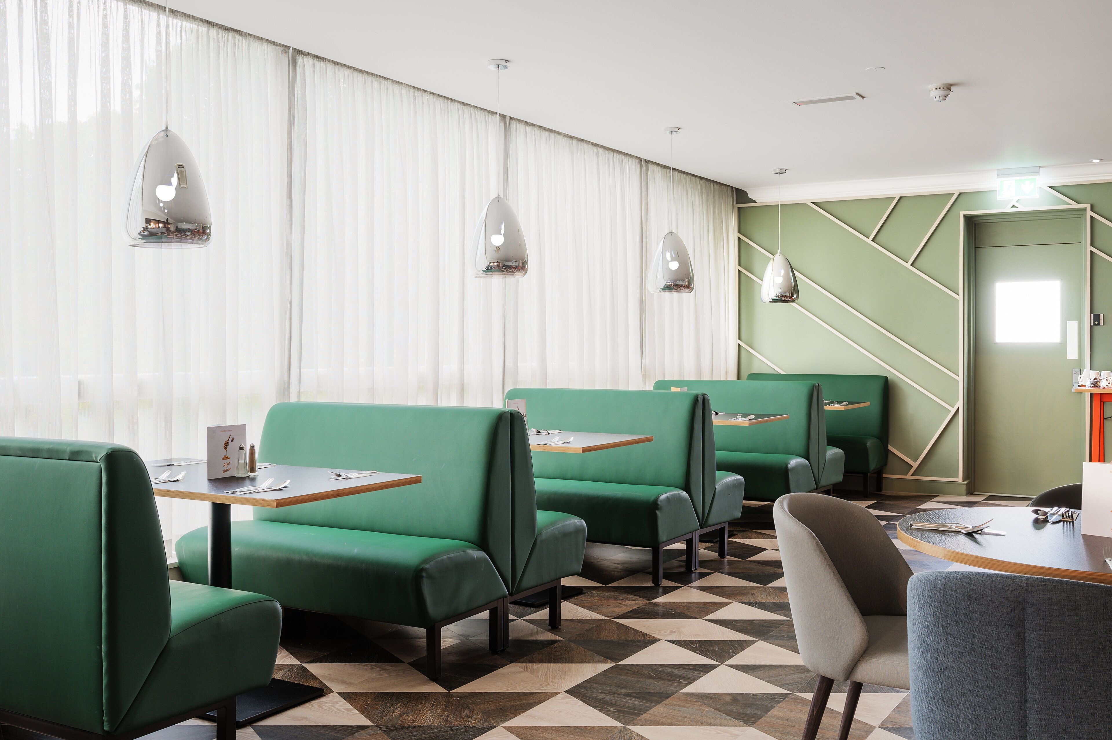 A modern hotel lobby with green seating, a check-in counter, and a geometric patterned floor.