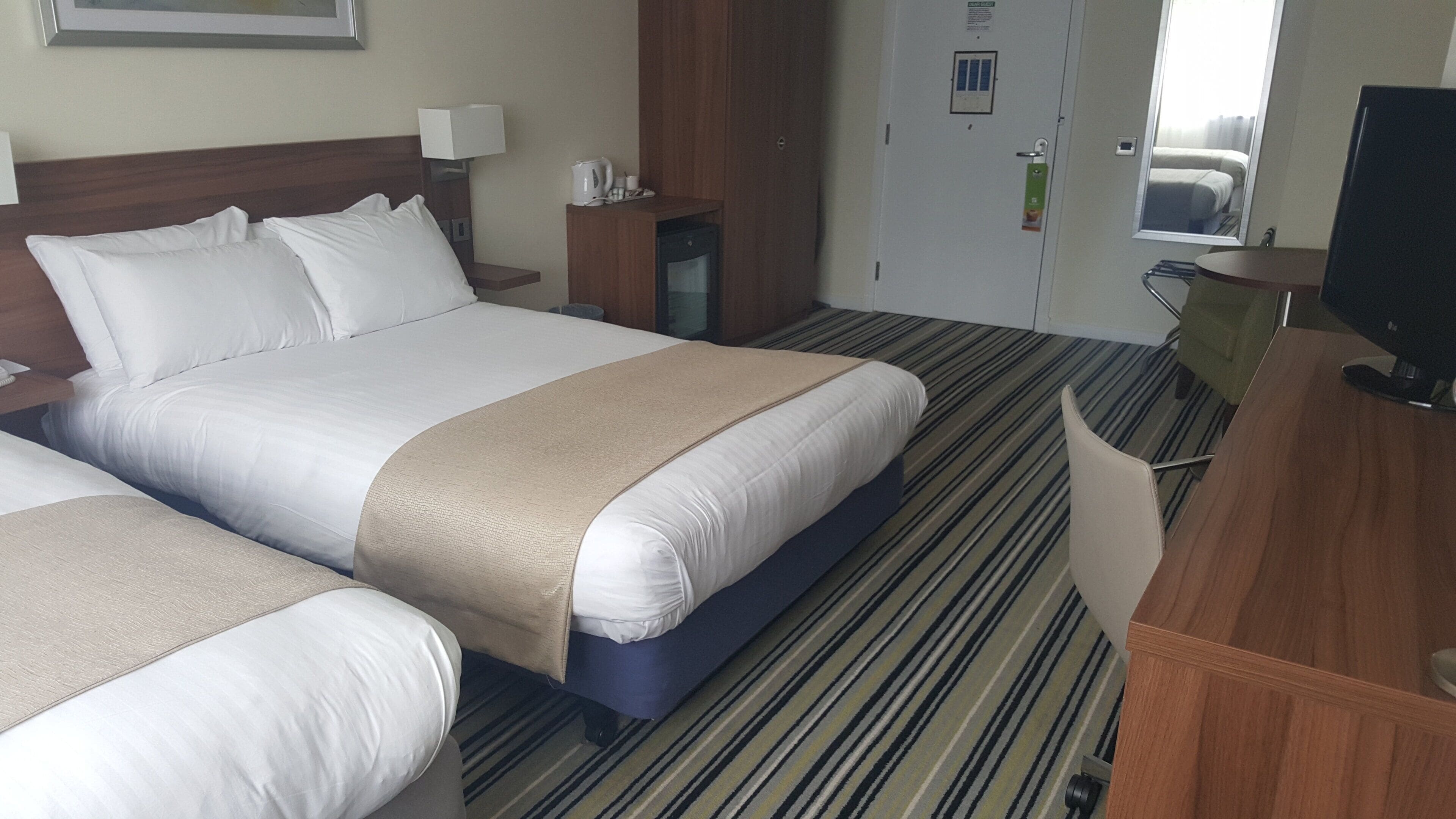 A hotel room with a large bed, a desk, a chair, and a television.