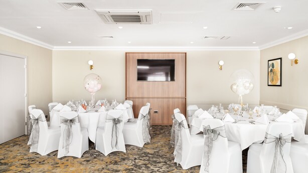 A conference room with white tables and chairs, a wooden door, and a mounted flat-screen TV. - Holiday Inn Derby Nottingham M1 J25 by IHG (Nottingham)
