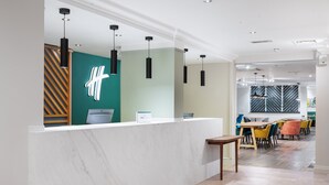 A modern reception area with a marble counter, pendant lighting, and a view into a dining area with colorful chairs and tables. - Holiday Inn Derby Nottingham M1 J25 by IHG (Nottingham)