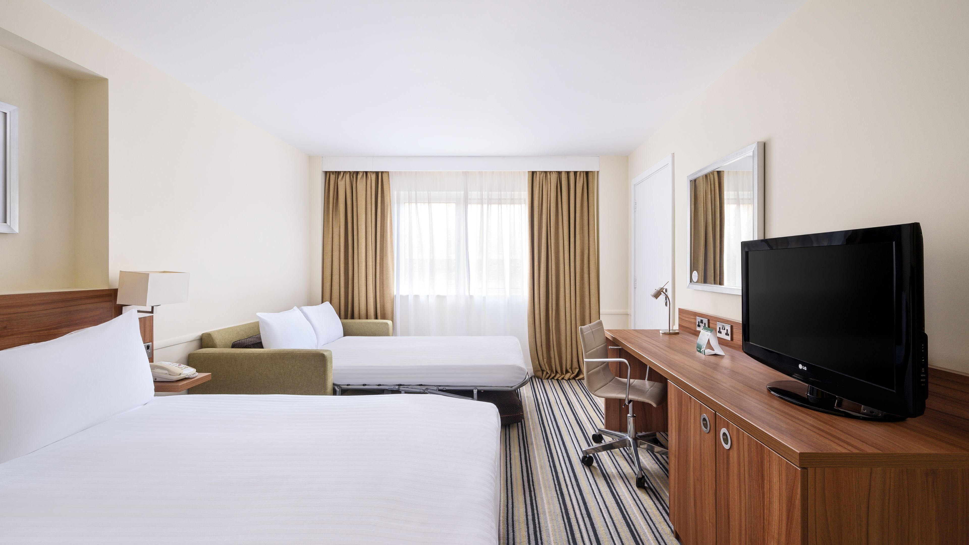 A hotel room with two beds, a desk with a TV, a chair, and a lamp.