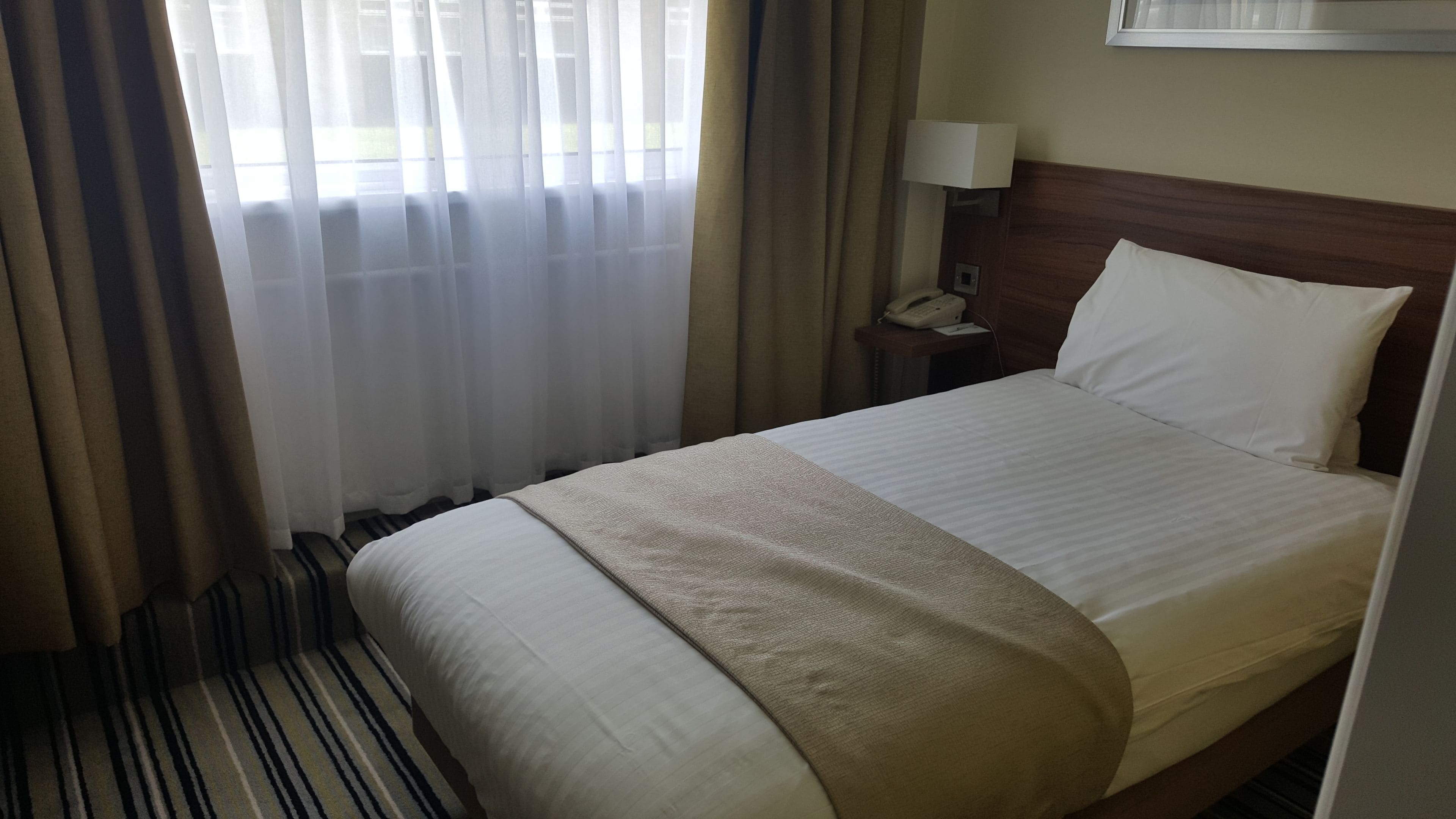 Ein Hotelzimmer mit einem Bett, einem Nachttisch mit Lampe und einem Telefon.
