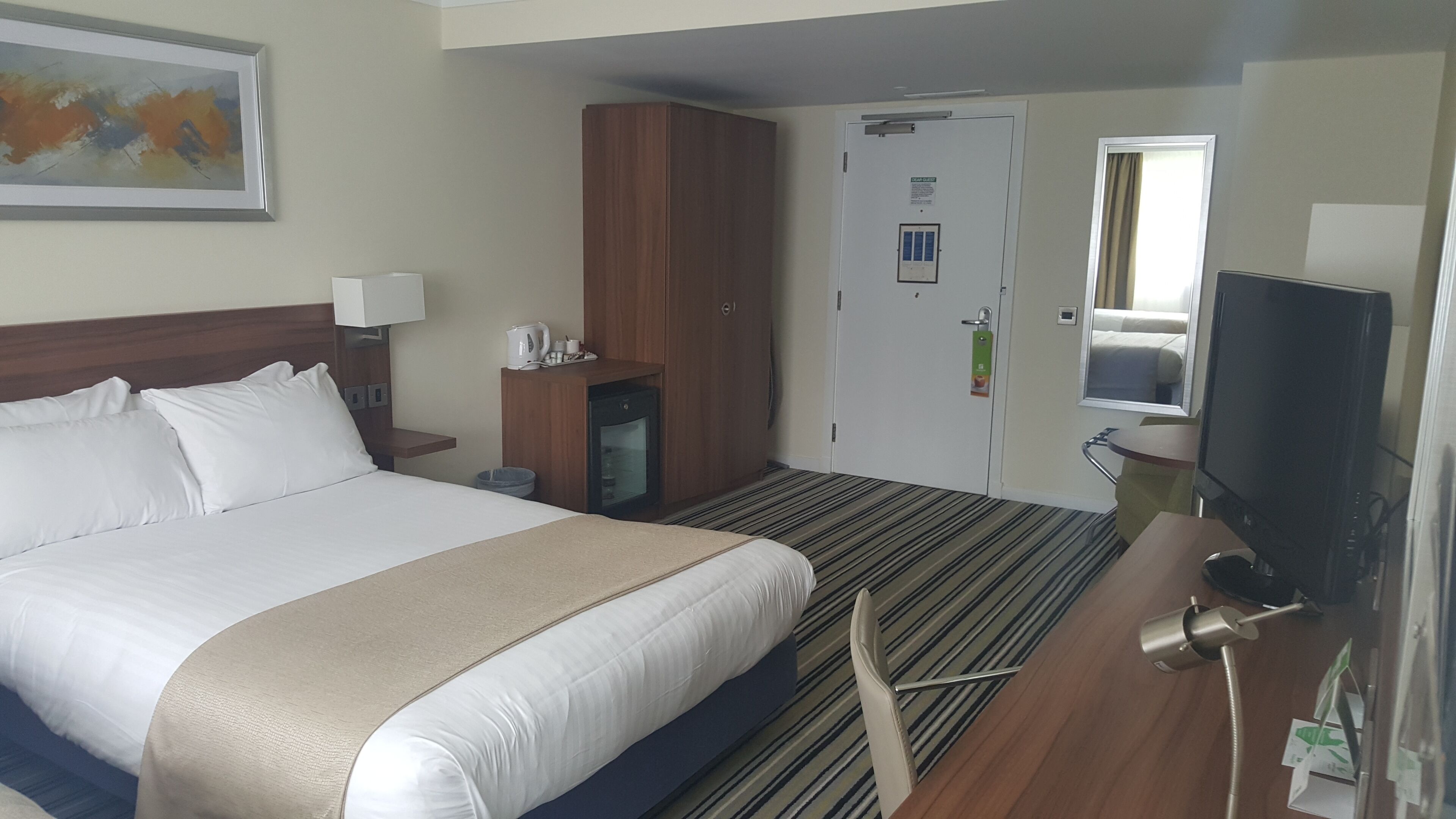 Una habitación de hotel con una cama grande, un armario de madera, un televisor y una pequeña kitchenette.