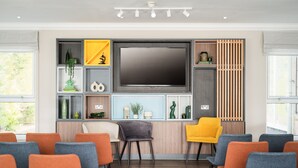 A conference room with a large flat-screen TV, multiple chairs, and a wooden panel wall with shelves. - Holiday Inn Derby Nottingham M1 J25 by IHG (Nottingham)