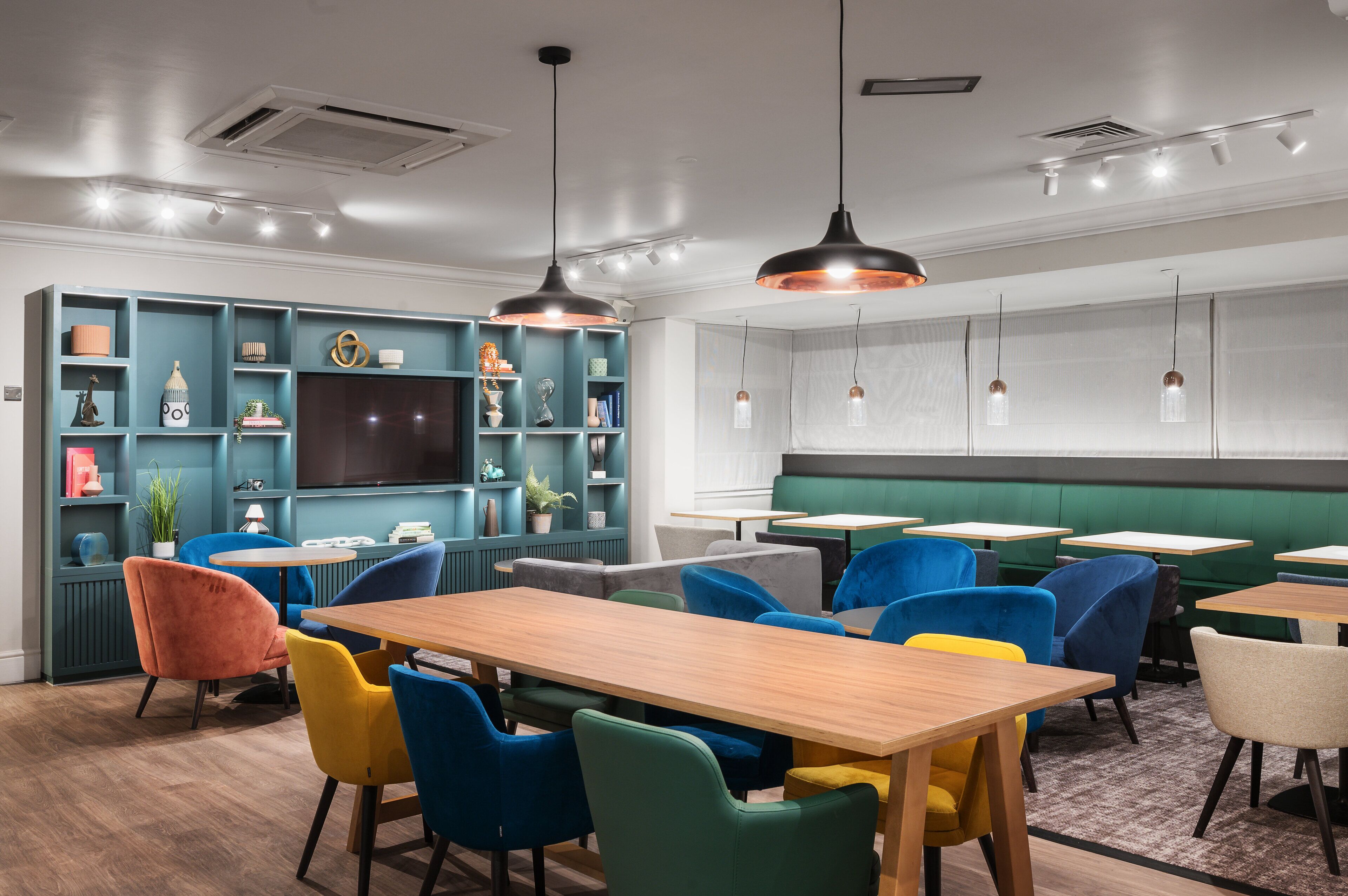 A modern dining area with colorful chairs, wooden tables, and pendant lighting.