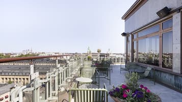 A rooftop terrace with outdoor seating, a large window, and a view of the cityscape.