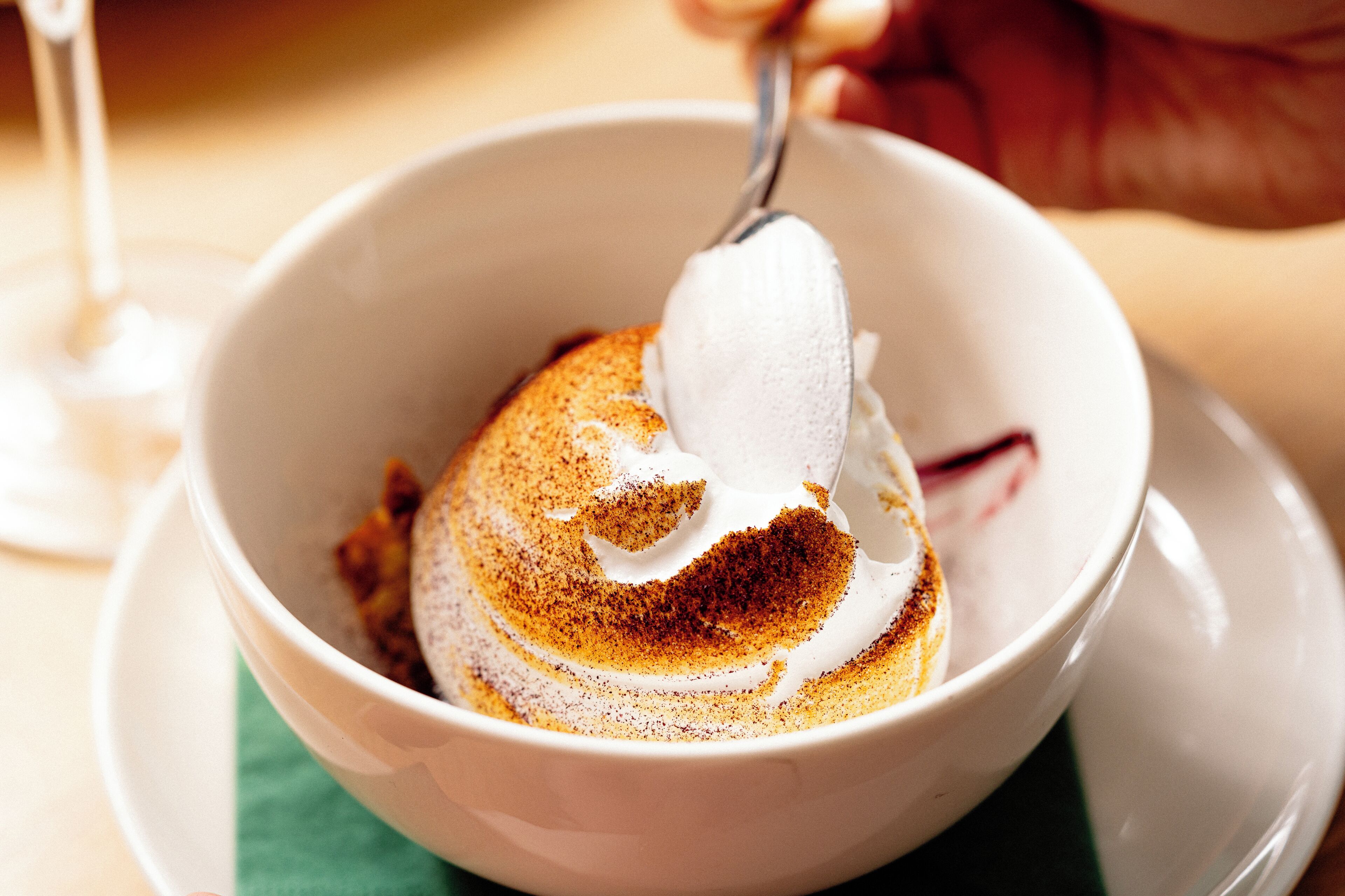 A white bowl with a dessert topped with whipped cream and a sprinkle of cinnamon.