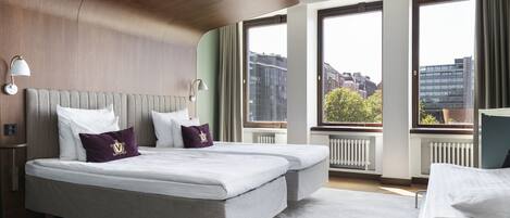 Habitación de hotel con una cama grande, dos mesitas de noche, un ventanal con vistas a la ciudad y techo de madera.