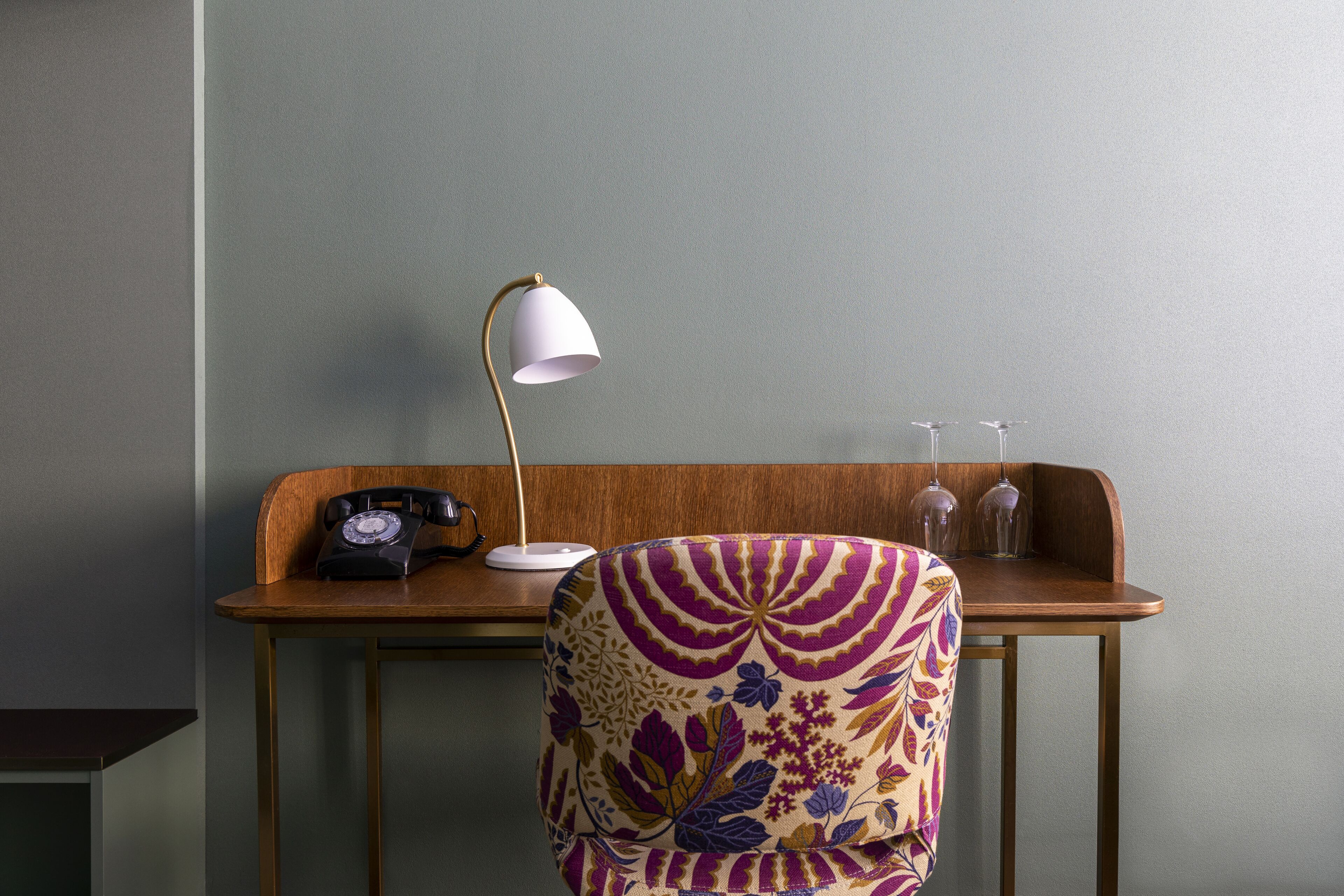 A desk with a telephone, a lamp, and a chair with a floral pattern.