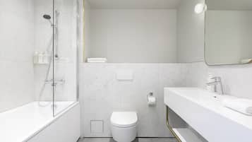 Un baño moderno con ducha envuelta en vidrio, inodoro blanco y tocador con lavamanos y espejo.