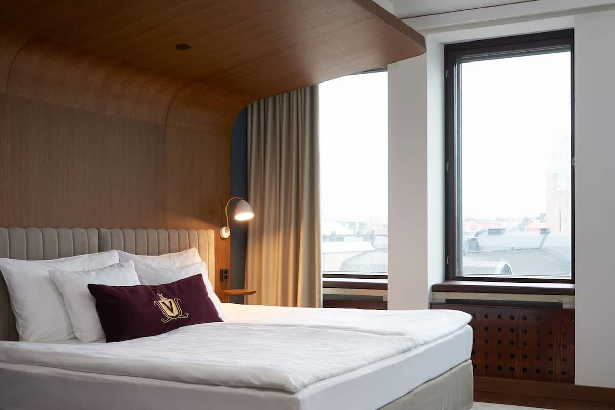 Una habitación de hotel con una cama grande, cabecera, ventana con vistas y una lámpara.
