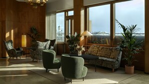 Amplia sala de estar con un ventanal que ofrece vista a la ciudad, un candelabro y varios sillones verdes y un sofá.