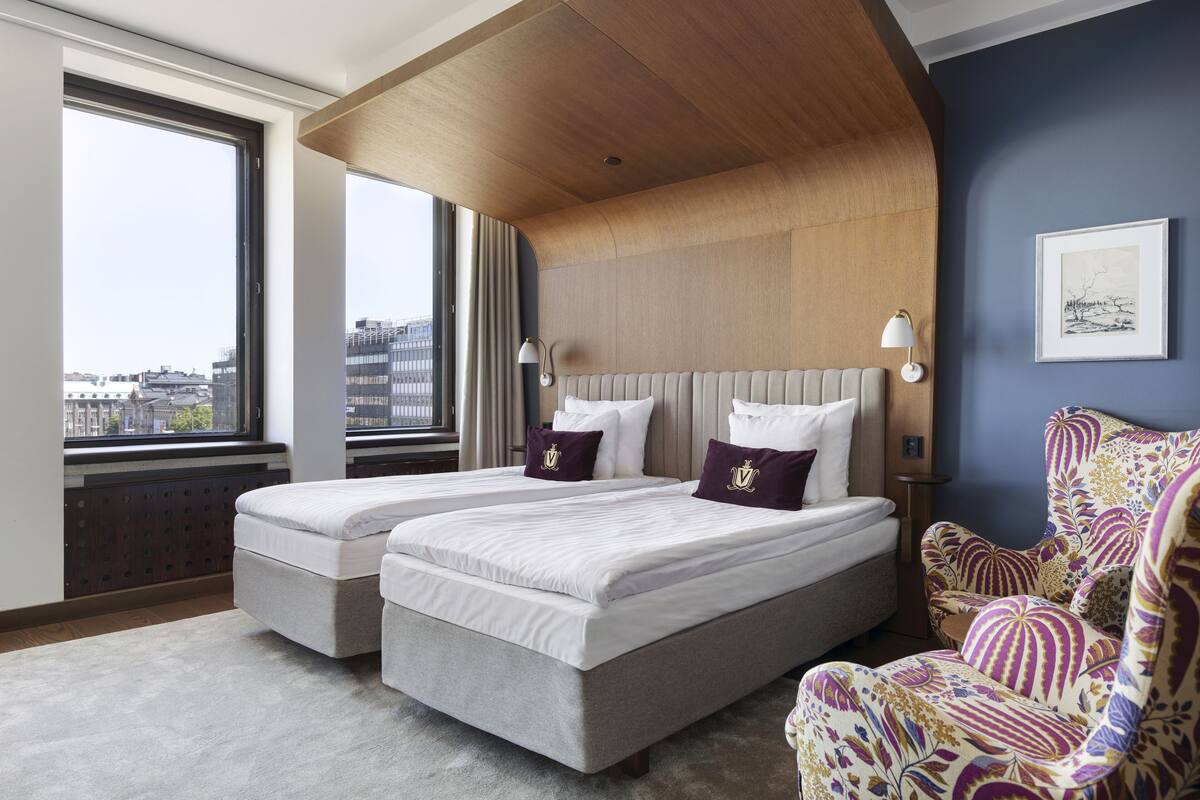 Una habitación de hotel moderna con dos camas, un ventanal grande y vistas a la ciudad.