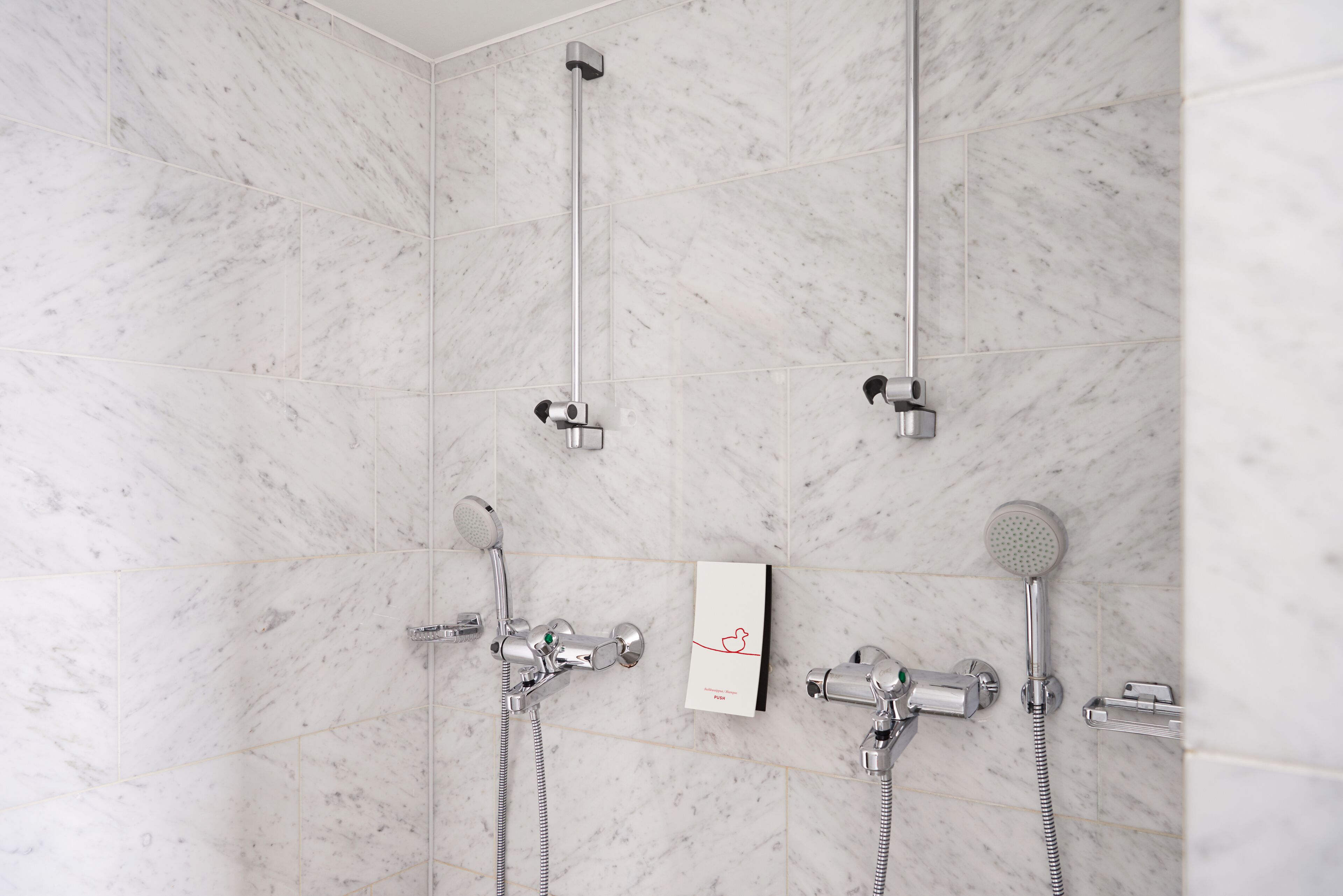 A modern bathroom with a marble floor and walls, featuring a shower with a handheld showerhead and a wall-mounted faucet.