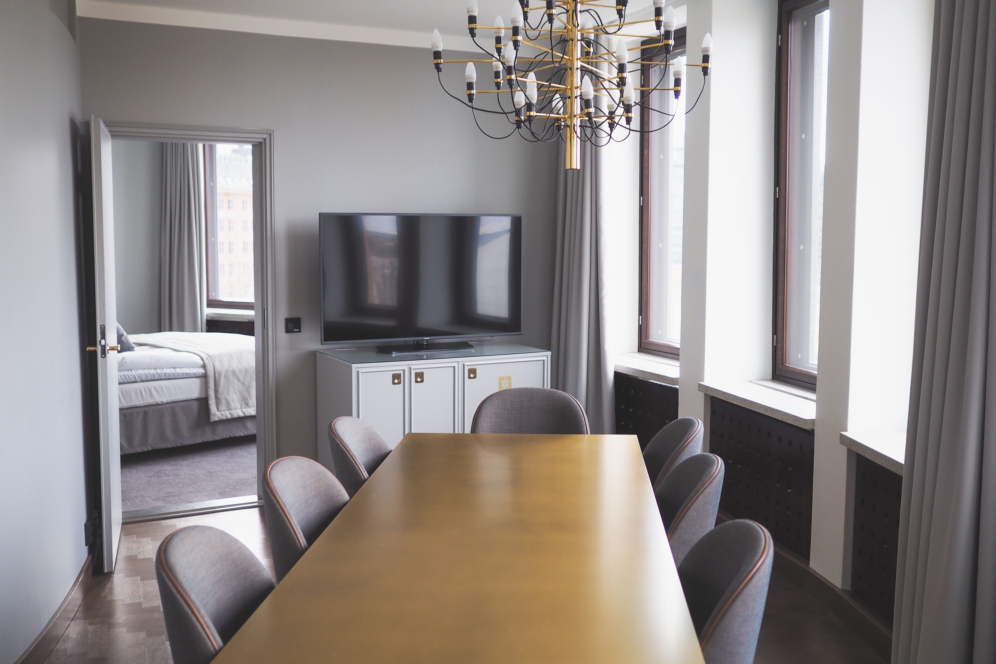 A hotel room with a dining table, chairs, a television, and a bed.