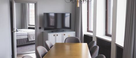 A hotel room with a dining table, chairs, a television, and a bed.