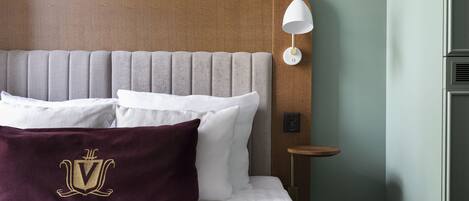 A neatly made bed with white and maroon pillows, a wooden headboard, and a bedside table with a lamp.