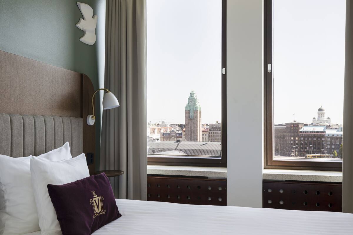 Una habitación de hotel con una cama grande, vistas de la ciudad a través de la ventana y un adorno en la pared.